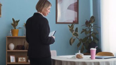 Orta yaşlı, Kafkas sosyal hizmetler görevlisi siyah bir elbise içinde daireyi teftiş ederken ve notlar alırken orta boy bir fotoğraf.