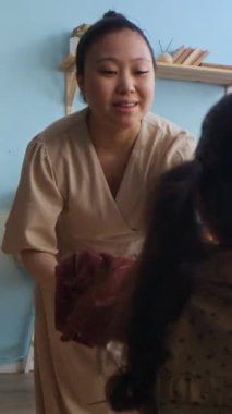 Küçük Asyalı bir kızın hamile bir anneye, oturma odasındaki çekmecelere çamaşır koyarken çekilmiş dikey bir fotoğrafı.