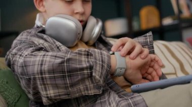 Kafkasyalı çocuk kulaklık takıp akıllı kasetini kontrol ediyor ve akıllı telefonuyla koltukta rahatça oturuyor, evde boş zamanlarında dinleniyor.
