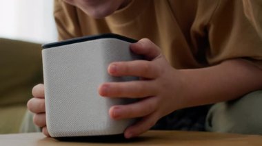 Beyaz gen z çocuk akıllı konuşmacı ile etkileşim, ses komutu verir ya da sıcak ev ortamında soru sorar