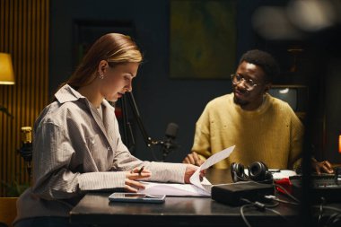 Stüdyoda masada oturan meslektaşlar podcast 'ten ya da stüdyodaki röportajdan önce kağıt üzerinde metin okuyorlar.