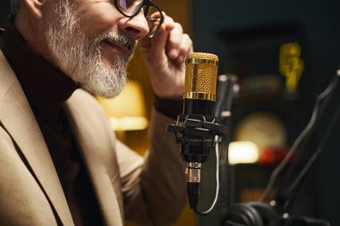 Stüdyoda online podcast sırasında mikrofonla konuşan olgun bir adam.