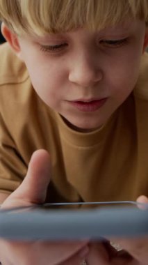 Akıllı telefonuyla derinden meşgul genç beyaz bir çocuk dikey olarak, dikkatle kayarken ekrana bakıyor.