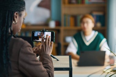 Modern ofis ortamında arka planda bulanık derinlik veren erkek arkadaşını kaydetmek ya da fotoğraflamak için akıllı telefon kullanan bir kadın. İşle ilgili aktiviteleri yakalamaya odaklan