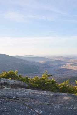 Acadia Ulusal Parkı 'ndaki kayalık bir dağın tepesinden bir manzara. Dağlar vadiyi gölgeleyecek ve yemyeşil çalılar güneş ışığında parlayacak..
