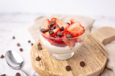 Vanilyalı yoğurt kasesi üzerine taze çilek ve şekersiz çikolata parçacıkları..