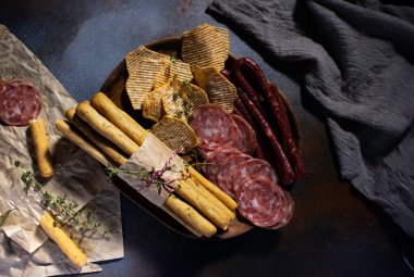 Kaba bir sonbahar şarküteri tabağı içinde salchichon, grissini ve koyu beton bir masa üzerinde tüm tahıl parçaları var..