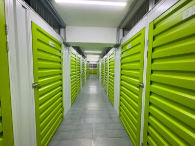 Parlak yeşil metal kapıları ve fayanslı zemini olan modern bir depolama koridorunun geniş açılı görüntüsü. Güvenlik, organizasyon ve depolama çözümleri için ideal temiz, iyi ışıklandırılmış alan.