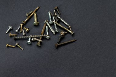 Farklı boyutlarda ve şekillerde küçük vidaların koyu bir arka planda dağılması