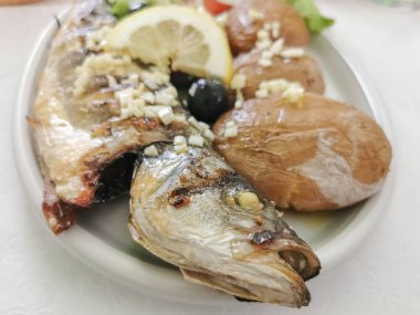 Tabak yemek, sebze salatası ve patatesle doldurulmuş sağlıklı ızgara uskumru tabağı, batata a a murro, Portekiz tipik yemek, dilimlenmiş domates, marul, soğan, zeytin ve limon.