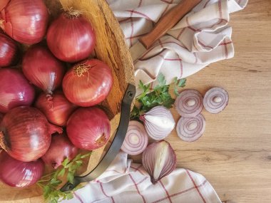 Photo composition view with whole onions in traditional wooden bowl, background with wooden table and sliced onions, parsley branch, kitchen towel and knife...