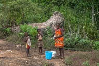 Conda Sumbe Angola - 02: 25: 2020: Geleneksel Angola kabile ailesinin yolu üzerindeki görüntüsü, 3 çocuklu bir anne, biri annesinin sırtında, fakir ama mutlu bir aile, tropikal ormanın ortasında.