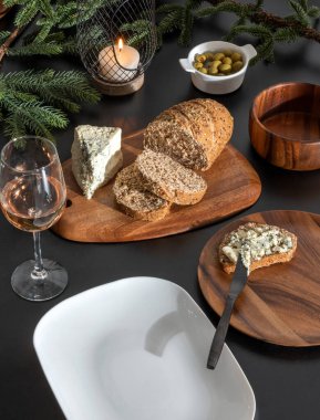Lezzetli Akdeniz atıştırmalıkları, sağlıklı zanaatkar tam tahıllı ekmek dilimleri, keçi peyniri ve siyah bir masada modern ahşap yemek tabağında yer alan zeytinler.