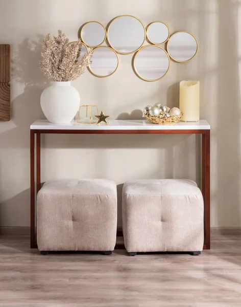 stock image Cozy living room interior featuring a wooden console table with household ornaments and beige cube ottomans, a hanging mirror on a beige wall