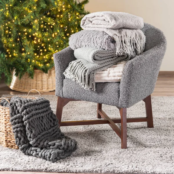Cozy Nordic Winter Living Room with Grey Armchair, Warm Folded Blankets, Knitted Plaids, Illuminated Christmas Tree, All in Natural Light & Neutral Colors