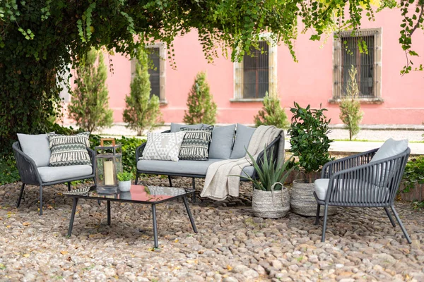 Outdoor boutique hotel patio in the garden with a grey sofa set with pillows and chairs on a cobbled floor
