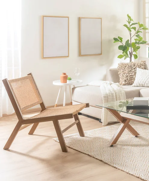 Stock image Interior of a Minimalist Mid-Century Living Room with a Rattan Lounge Chair Beside a Chaise Longue Sofa, Coffee Table, and Mock-Up Poster Frame on a White Wall, over Wooden Flooring.