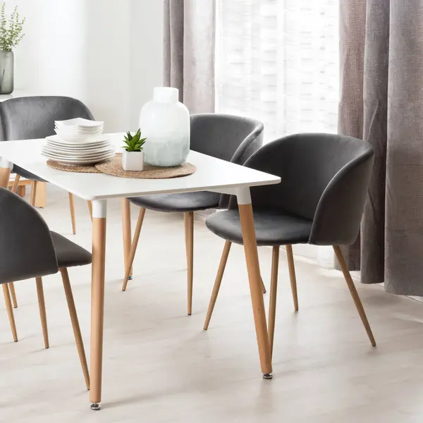 Bright Modern Dining Room with Wood-Legged White Table, Grey Fabric Chairs, White Dinnerware, Home Decor, Natural Light from a Window, and Wooden Flooring.