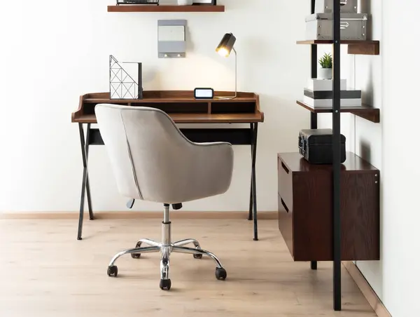 Interior of a Modern Office Featuring a Workstation with a Wooden Writing Desk with Work Tools, a Fabric Office Chair, and a Wooden Modular Shelving Unit for Storage, on Wooden Flooring.