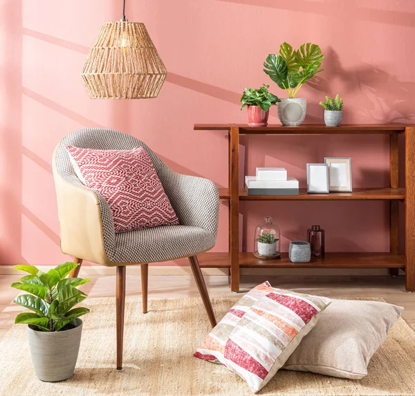 Living Room Interior with Linen Accent Sofa Seat, Decorative Pink Throw Pillows, shelf Bookcase, Rattan Hanging Lamp, Potted Plants. Sunlit Room with Window Shadows on Salmon Pink Wall, Spring Style.