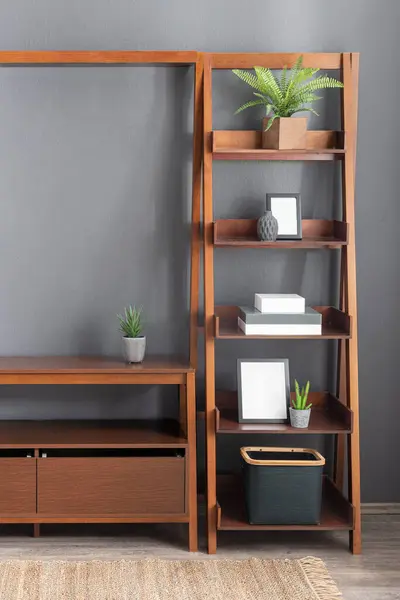 Wooden Nordic Ladder Bookshelf Display Cases with Drawer, Books, Blank Picture Frames, and Decorative Plants in Modern Living Room. Light Gray Wall and Hardwood Flooring with Area Rug.