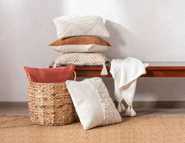 Decorative Wicker Baskets with Set of Cotton Throw Square Pillows and Cushion Covers, White Woven Throw Blanket on a Rectangular Wooden Accent Bench, in a Bright Room with an Area Rug on the Floor.