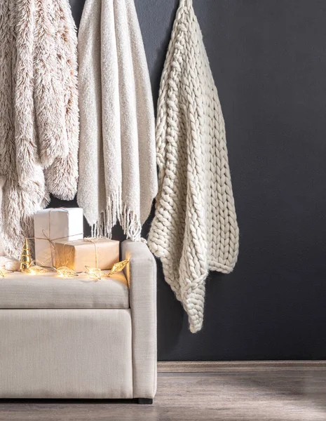 Cozy Corner with Neutral-Toned Throws blankets Hanging on a Dark Wall, Light Beige bench Sofa Adorned with Wrapped Presents and Glowing Fairy Lights, Chunky Knit and Fluffy Textures, Wooden Floor.