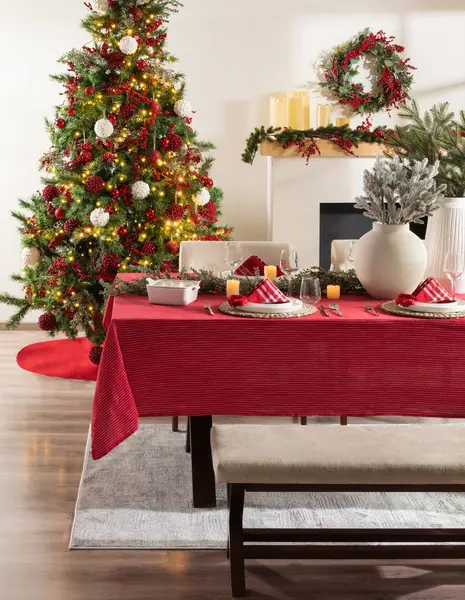 Gala Christmas Feast Setup, Dark Wood Table with Red Corduroy Tablecloth, White Ceramic Centerpiece, Beige Upholstered Bench, and a Tree with Red Ornaments, Fireplace with Festive Garland and Wreath.