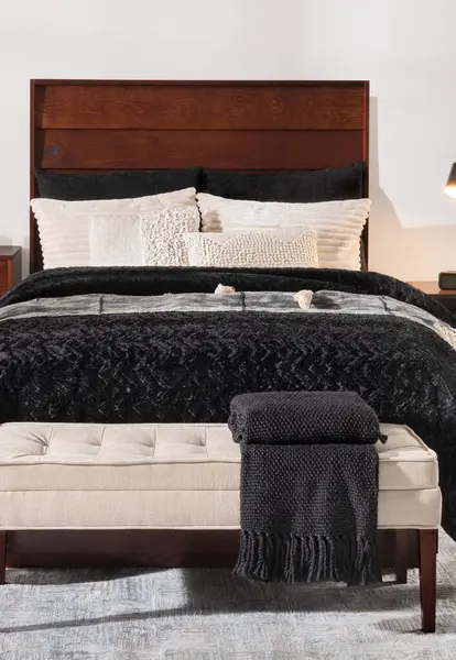 Nordic Bedroom Serenity: Rich Walnut Bed Frame with an Array of Textured Pillows, Black Knit Throw Blanket, Cream Fabric Bench with Charcoal Woolen Blanket, Set Against a Calm Neutral Palette.