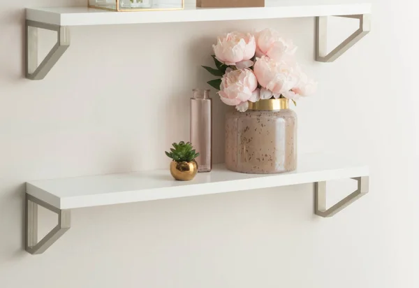 Elegant Floating Shelves Display: A Chic Ceramic Vase with Blush Pink Peonies, a Petite Glass Bottle, and a Small Gold Pot with a Succulent, Creating a Serene and Stylish Wall Accent in a Modern Home.