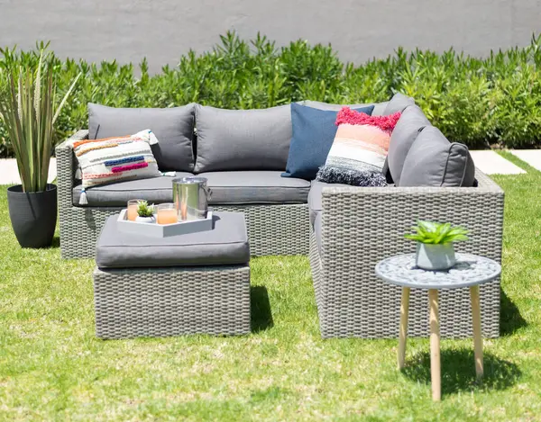 Inviting Outdoor Lounge Area with a modern Grey Wicker Sofa Set, a Love Seat and Armchairs with Accent Pillows, a Ottoman Serving as a Centrepiece Tray Table, a Circular Side Table, Set Upon a Lawn.