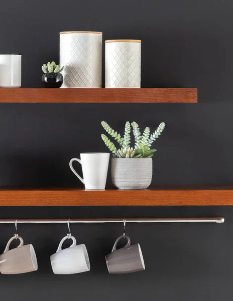 Sophisticated Kitchen Decor on Wooden Shelves: Embossed Ceramic Canisters, a Sleek White Cup, and a Modern Concrete Planter with Succulents, Paired with Hanging Mugs Below in a Chic Monochrome Palette