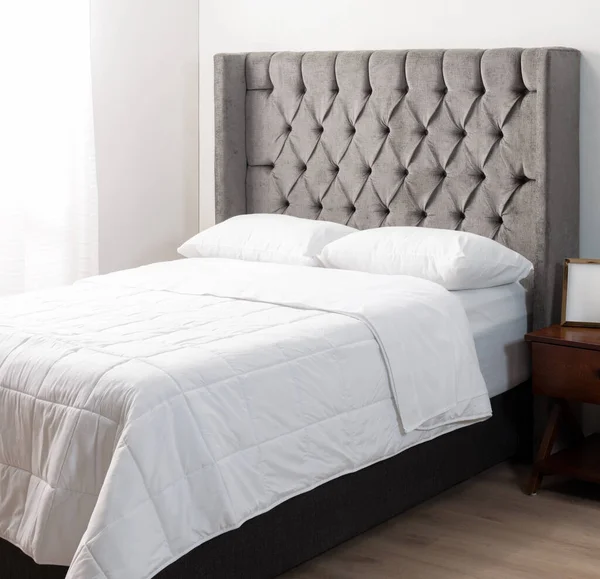Modern Bedroom Elegance: A Sophisticated Gray Tufted Headboard Complements the Clean Lines of a Dark Upholstered Bed, Accompanied by a Classic Wooden Nightstand and Crisp White Bedding, Restful.