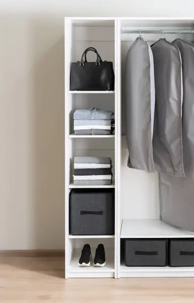 Wardrobe Organization: Bright White Closet Showcasing Neatly Folded Clothes on Shelves, Versatile Gray Storage Boxes, and Protective Garment Bags for Suit and Coat Storage in a Contemporary Bedroom.