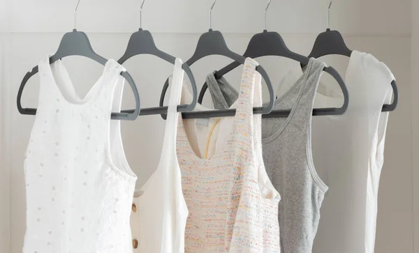 Array of Women\'s Summer Tops in Soft Neutral Hues, Delicately Draped on Dark Hangers Against a Pure White Closet Background, Emphasizing a Light, Airy, and Organized Wardrobe Aesthetic, Close up.