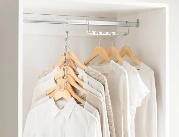 Cohesive Wardrobe Collection in Neutral Palette, Featuring a Variety of Textured Tops and Sweaters on Wooden Hangers, Neatly Organized in a Clean White Closet, Serene Clothing Storage Atmosphere.