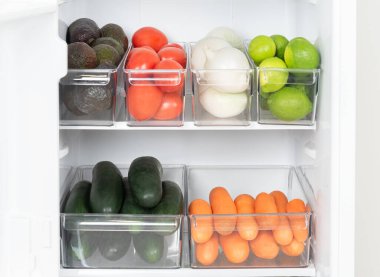 Sağlıklı meyve, sebze, avokado, domates, beyaz soğan, limon, sağlıklı yemek planlaması içeren şeffaf plastik kaplar içeren iyi organize edilmiş bir buzdolabı..