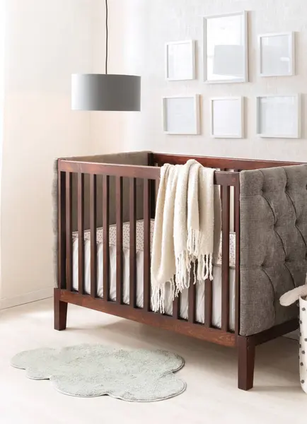 stock image Tranquil baby's bedroom featuring a mahogany traditional crib with a soft cream throw, a tufted gray wingback chair and whimsical cloud-shaped pale green rug. White empty photo frames adorn the wall.