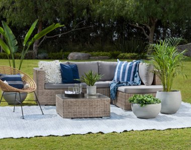 Relaxing garden lounge set against a lush landscape, with a rattan sectional sofa adorned with cozy cushions, complemented by a unique acapulco chair, and concrete planters adding a touch of greenery. clipart