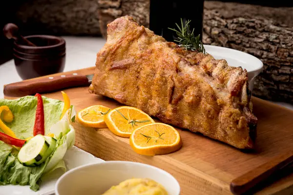 Tütsülenmiş domuz kaburgası ve ahşap tahtada biberiye - salata, patates püresi ve portakal dilimleri