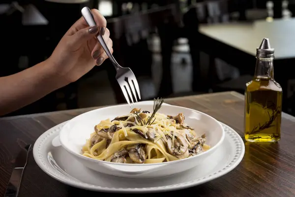 Lokantanın içinde lüks kremalı mantar fettuccine yemek. Genç bir kadının eli.