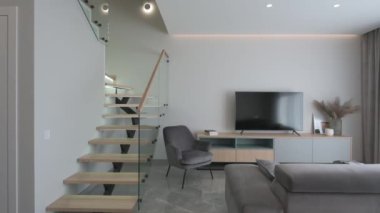Geniş, parlak İskandinav tarzı, cam elementleri ve gri bir kanepesi olan şık ahşap merdivenli bir oda. Yüksek kalite 4k görüntü