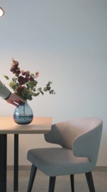 Bir adam ahşap bir masanın üzerine cam mavi bir vazo koyar. Bir dizi döşeme sandalyesi. Yüksek kaliteli FullHD görüntüler