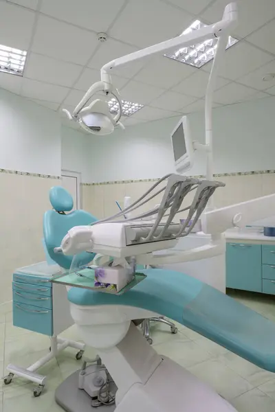 A modern dental office features a sleek blue and white dental chair. The metal frame gleams under the ceiling lights, creating a clean and professional atmosphere.