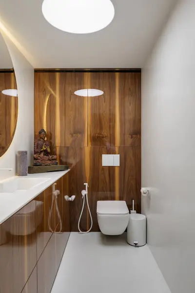 A bathroom in a building with wood cabinetry, sink and mirror. Features include property lighting fixtures, interior design elements, taps, and flooring