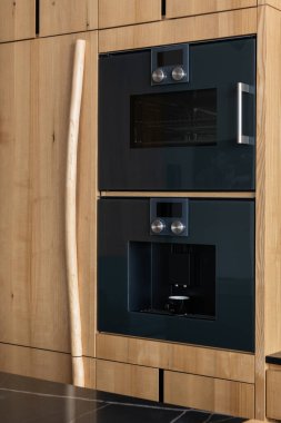 Ahşap döşeme, ahşap boyama rafları ve iki fırın ve mutfak aleti olarak da bir kahve makinesi olan bir dolap binasında bir mutfak.