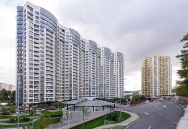 Bereketli yeşilliklerle çevrili modern gökdelenler şehrin üst kesimlerindeki bulutlu gökyüzüne ulaşır.