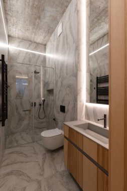 Zarif mermer duvarların, kaliteli ahşap dolapların ve şık aydınlatma armatürlerinin olduğu modern bir banyo.