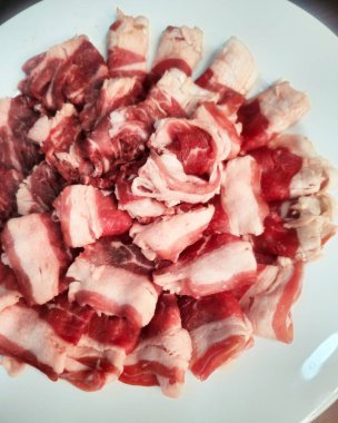 Beyaz tabakta dilimlenmiş çiğ domuz eti. Kapat..