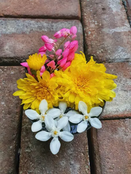 Flowers in a vase on the brick floor, Thailand. Bouquet of yellow flowers.
